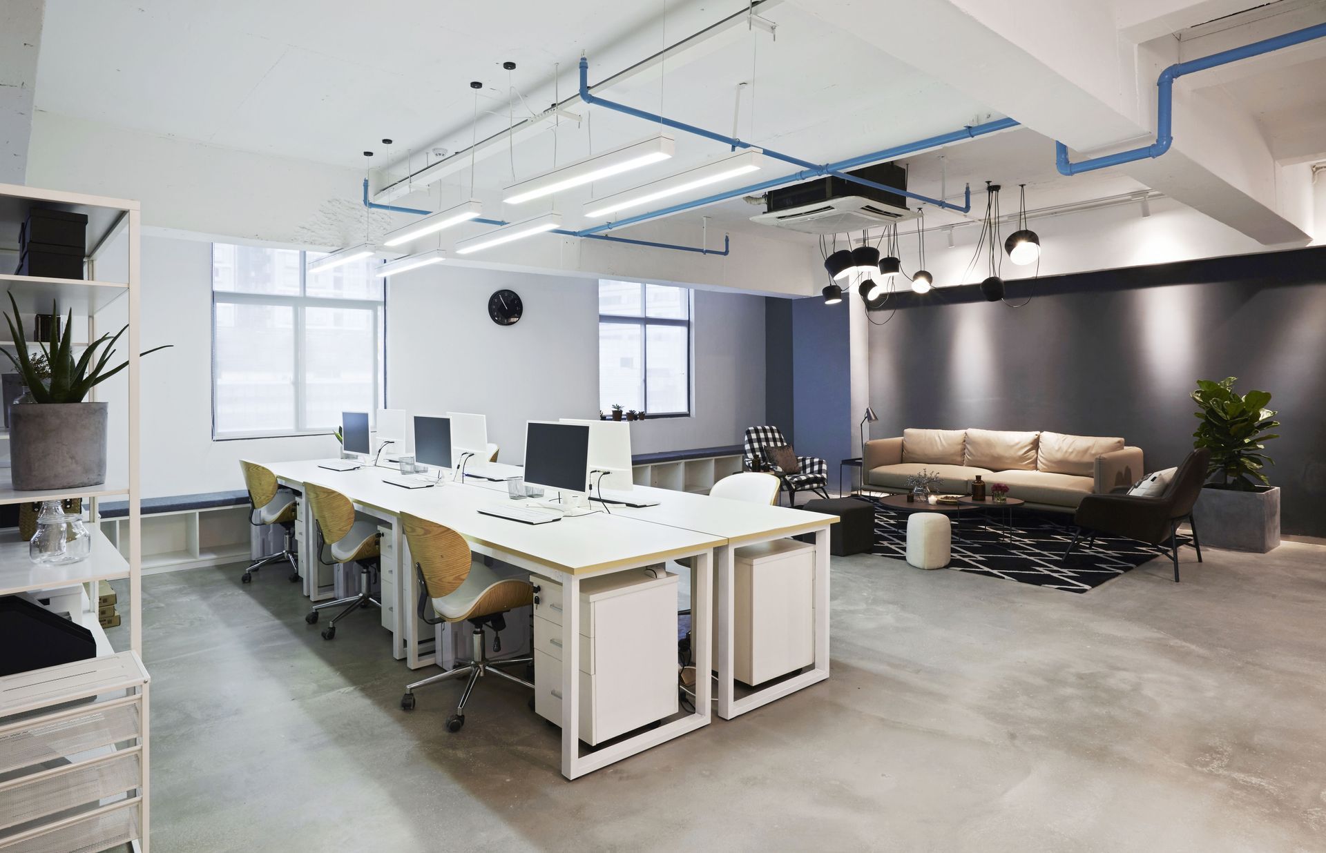 Modern open office with desks, chairs, couches, and large windows under bright ceiling lights
