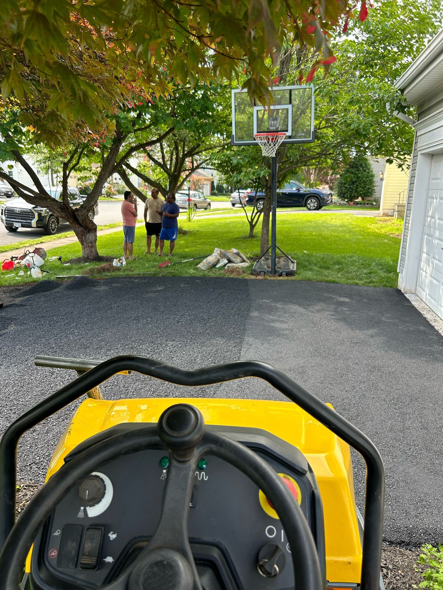 A yellow tractor is parked in a driveway next to a basketball hoop.