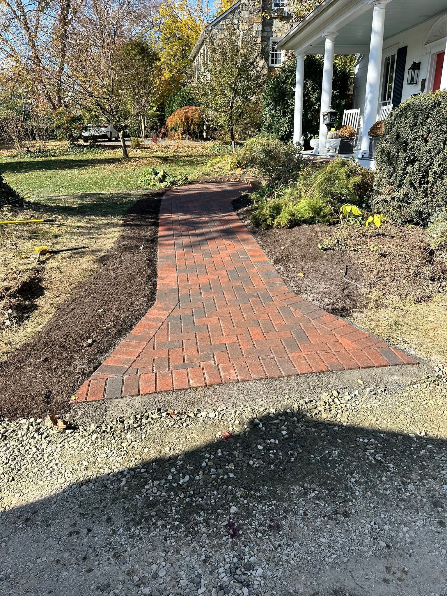 A brick walkway leading to a house with a porch.