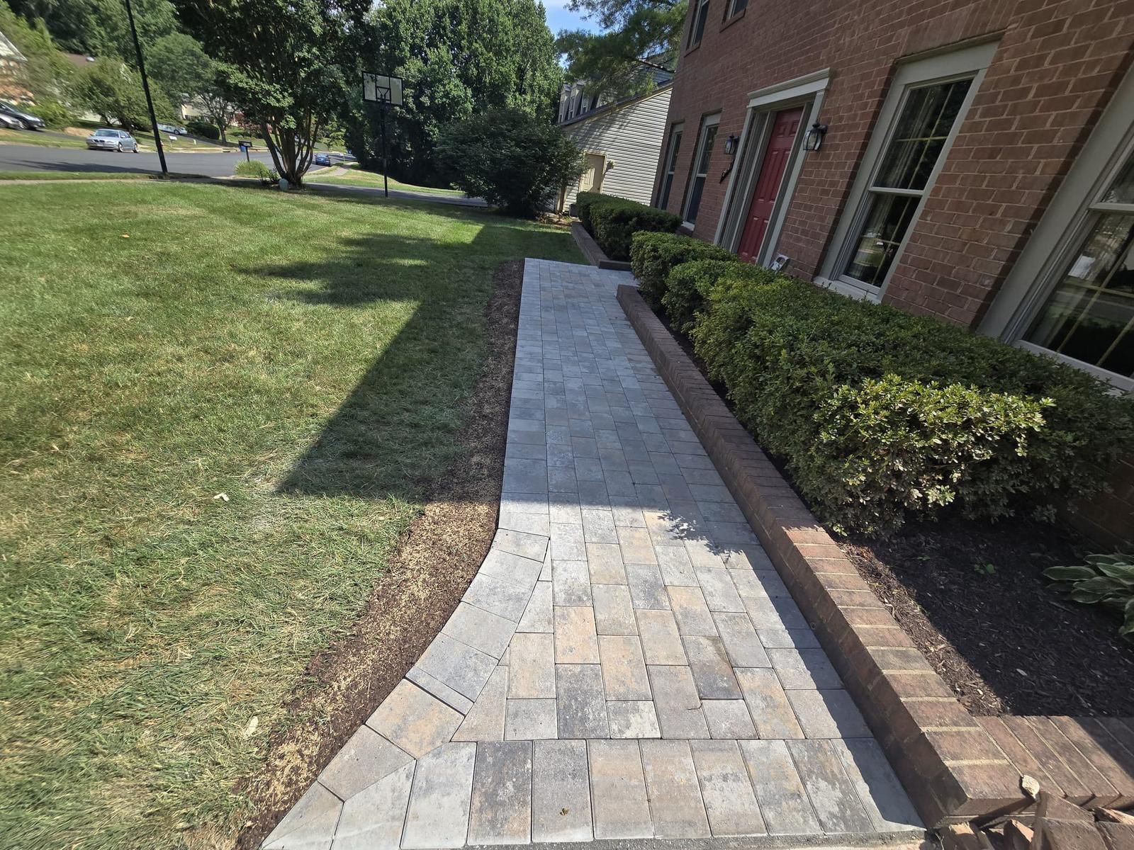 A sidewalk leading to a brick building with a red door