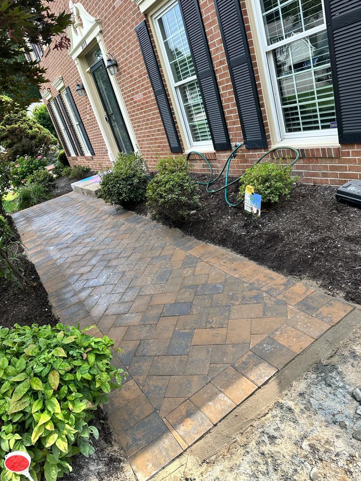 A brick walkway leading to a brick house with black shutters.