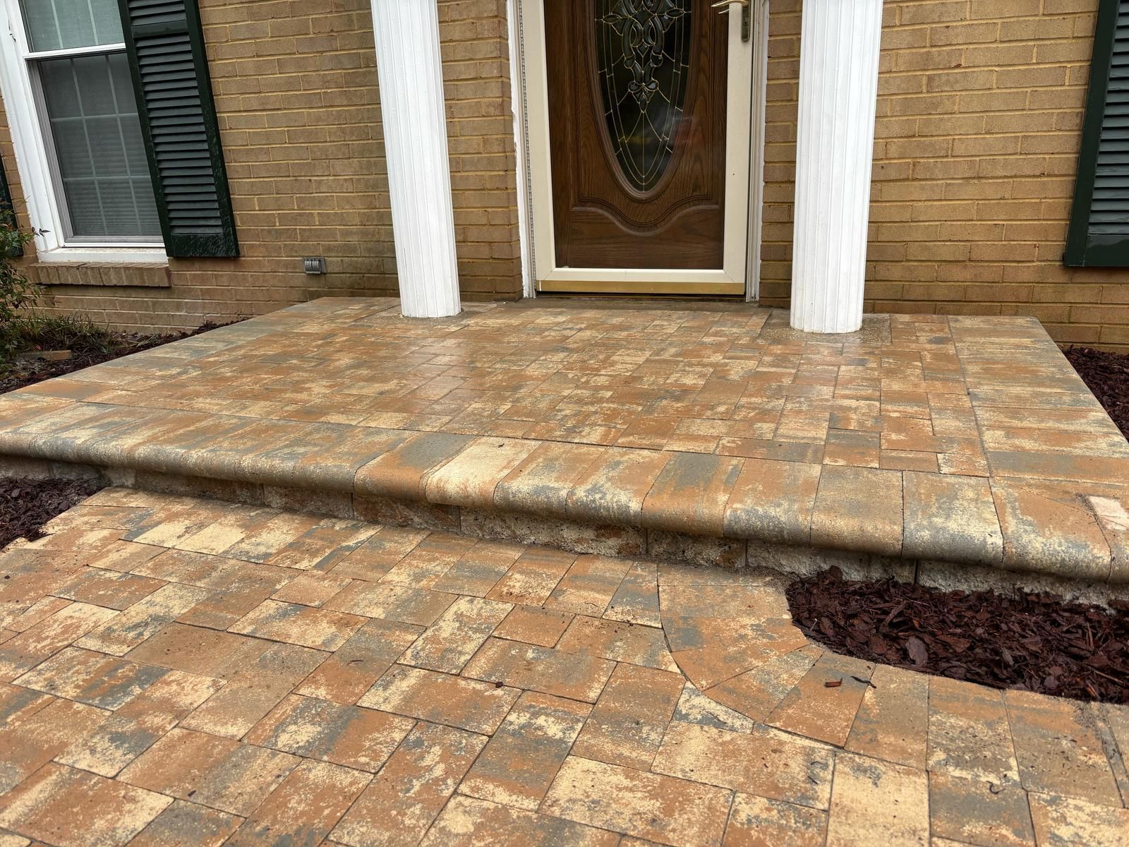 A brick porch with steps leading to the front door of a brick house.
