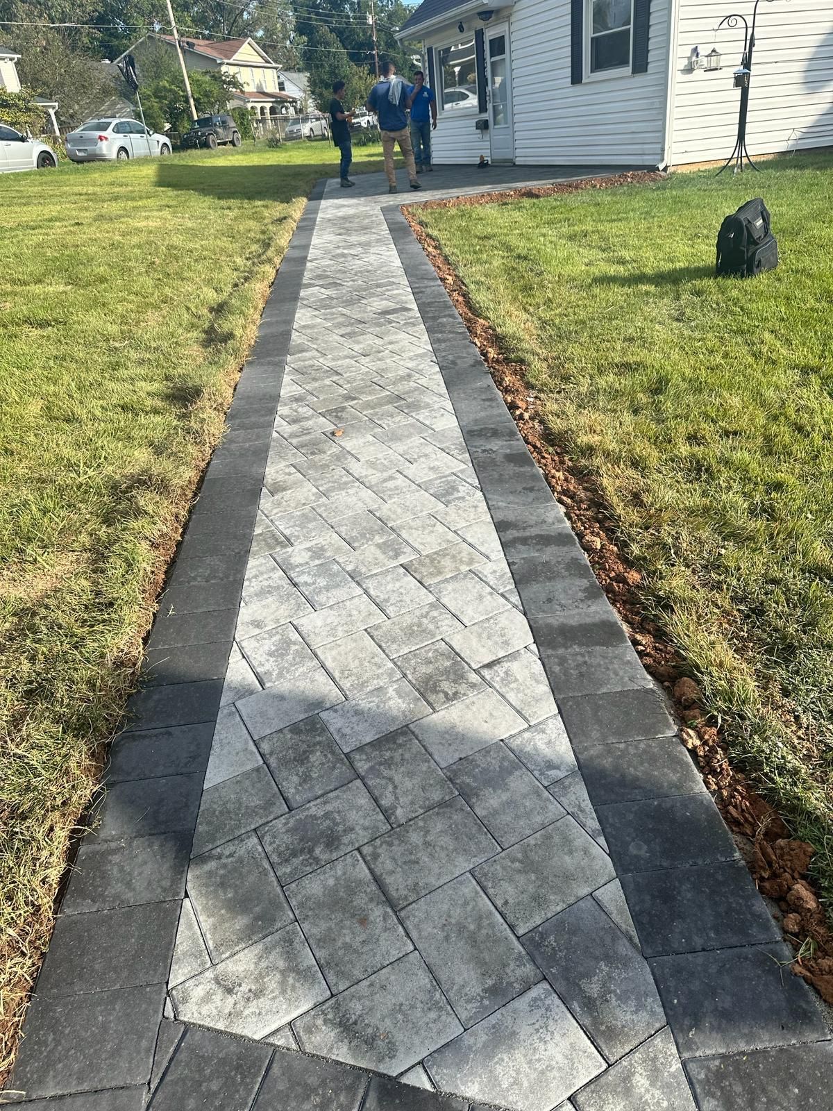 A brick walkway leading to a house with a lawn in the background.