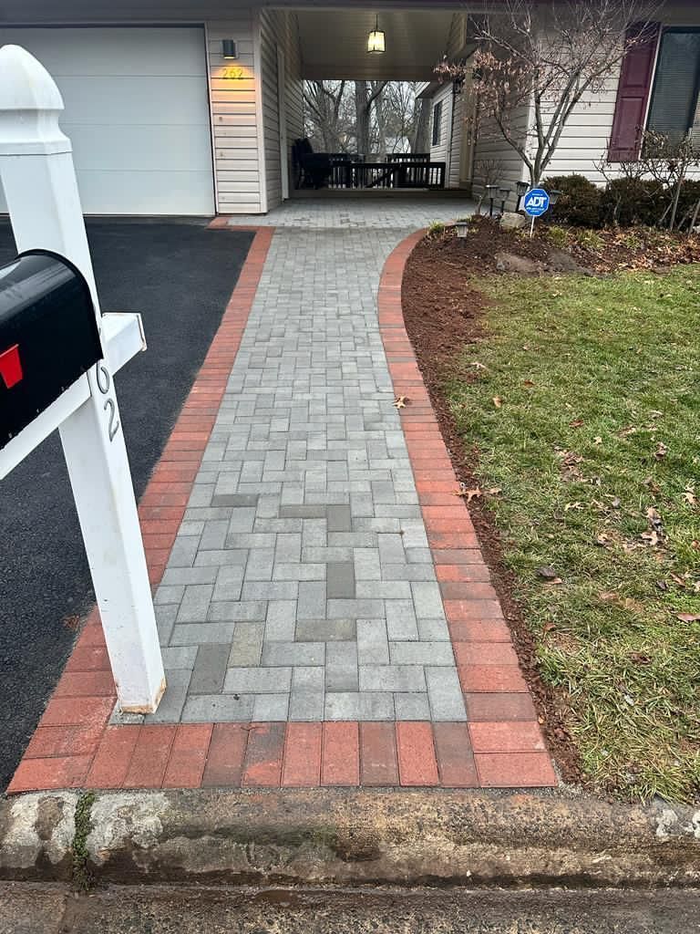 A brick walkway leading to a house next to a mailbox.