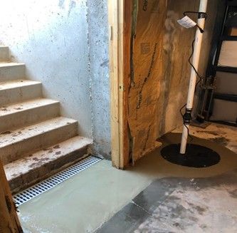 A basement with stairs and a drain in the floor.