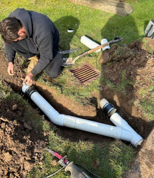 A man is kneeling down in the dirt working on a pipe