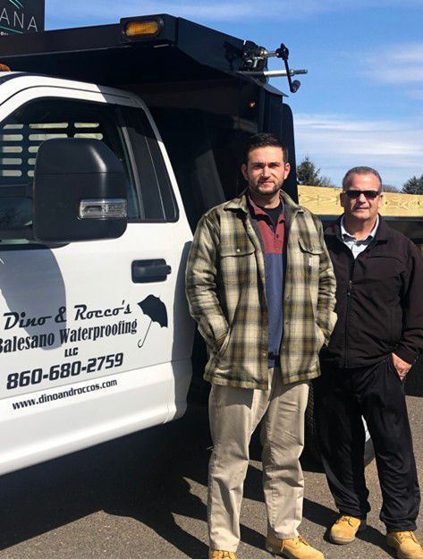 Two men are standing next to each other in front of a truck