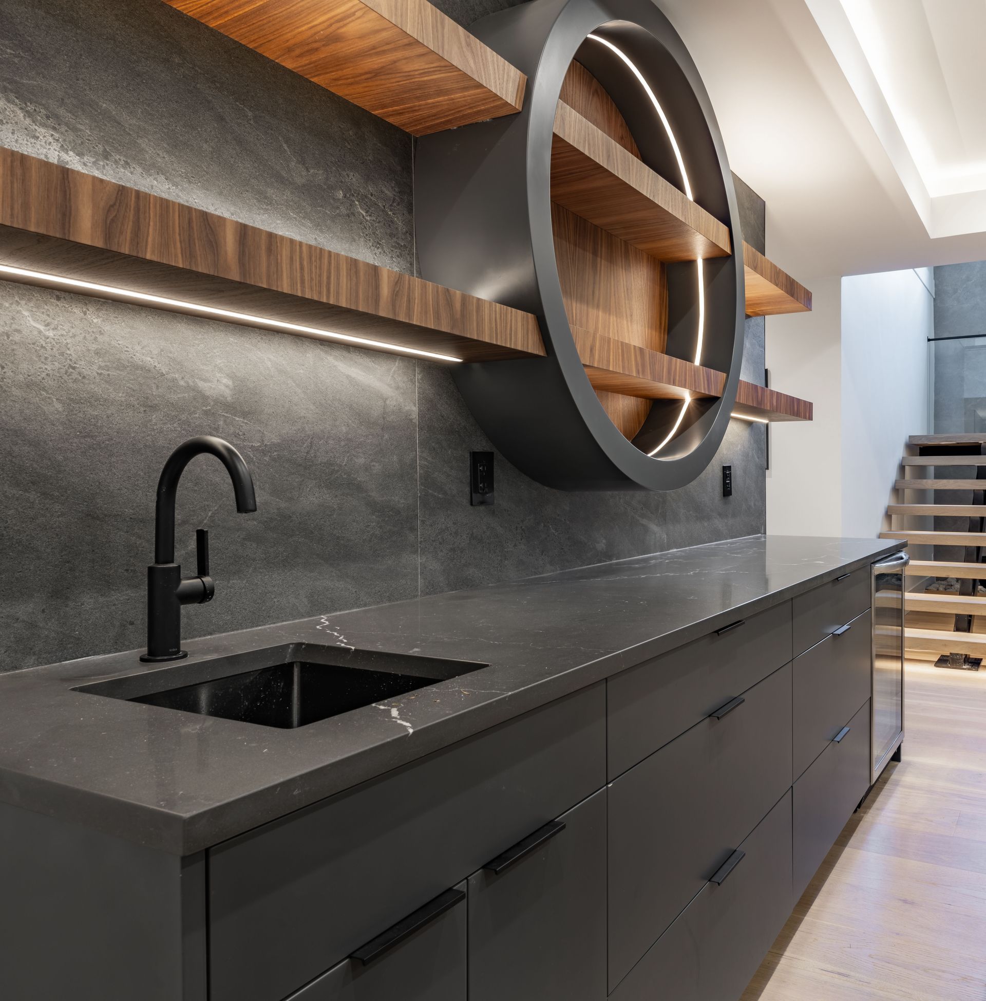 Modern kitchen with matte black cabinets, dark countertop, and circular wood wall shelves