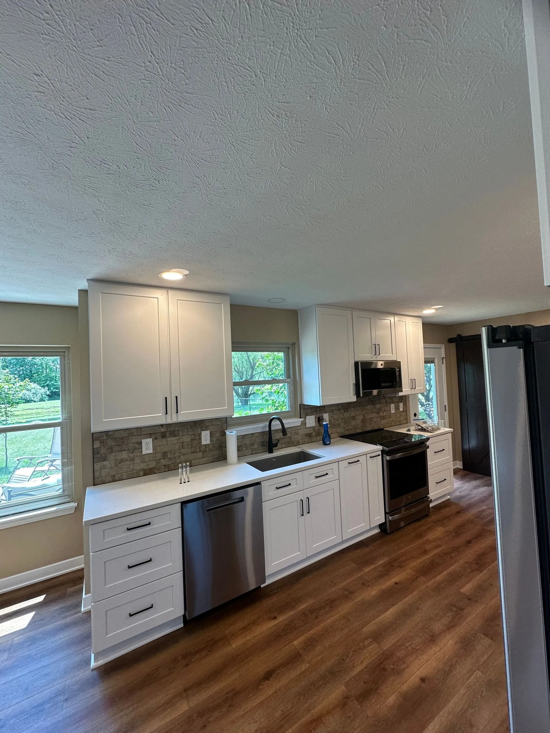 Bright kitchen with white cabinets, stainless appliances, and wood floors beside large windows