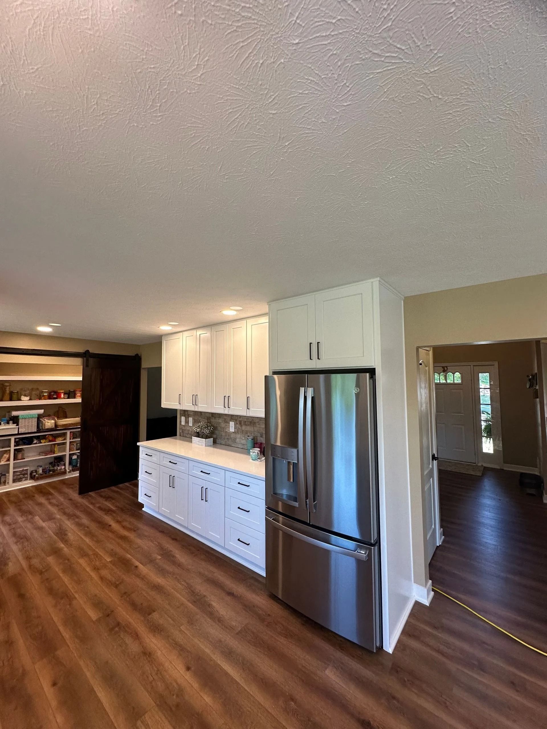 Bright kitchen with white cabinets, stainless fridge, wood floors, and view into adjacent dining room