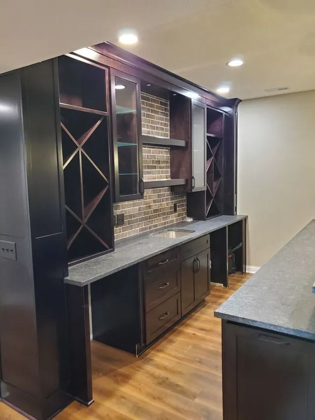 Built-in kitchen wet bar with dark cabinets, stone countertop, wine rack, and mosaic backsplash.