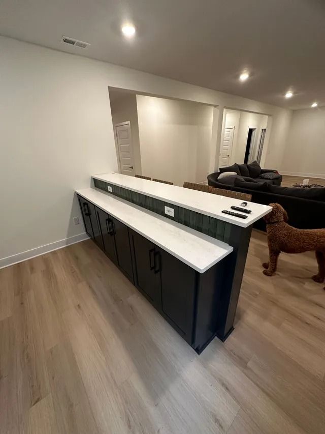 Modern kitchen with white countertops, dark cabinets, wood floors, and recessed ceiling lights