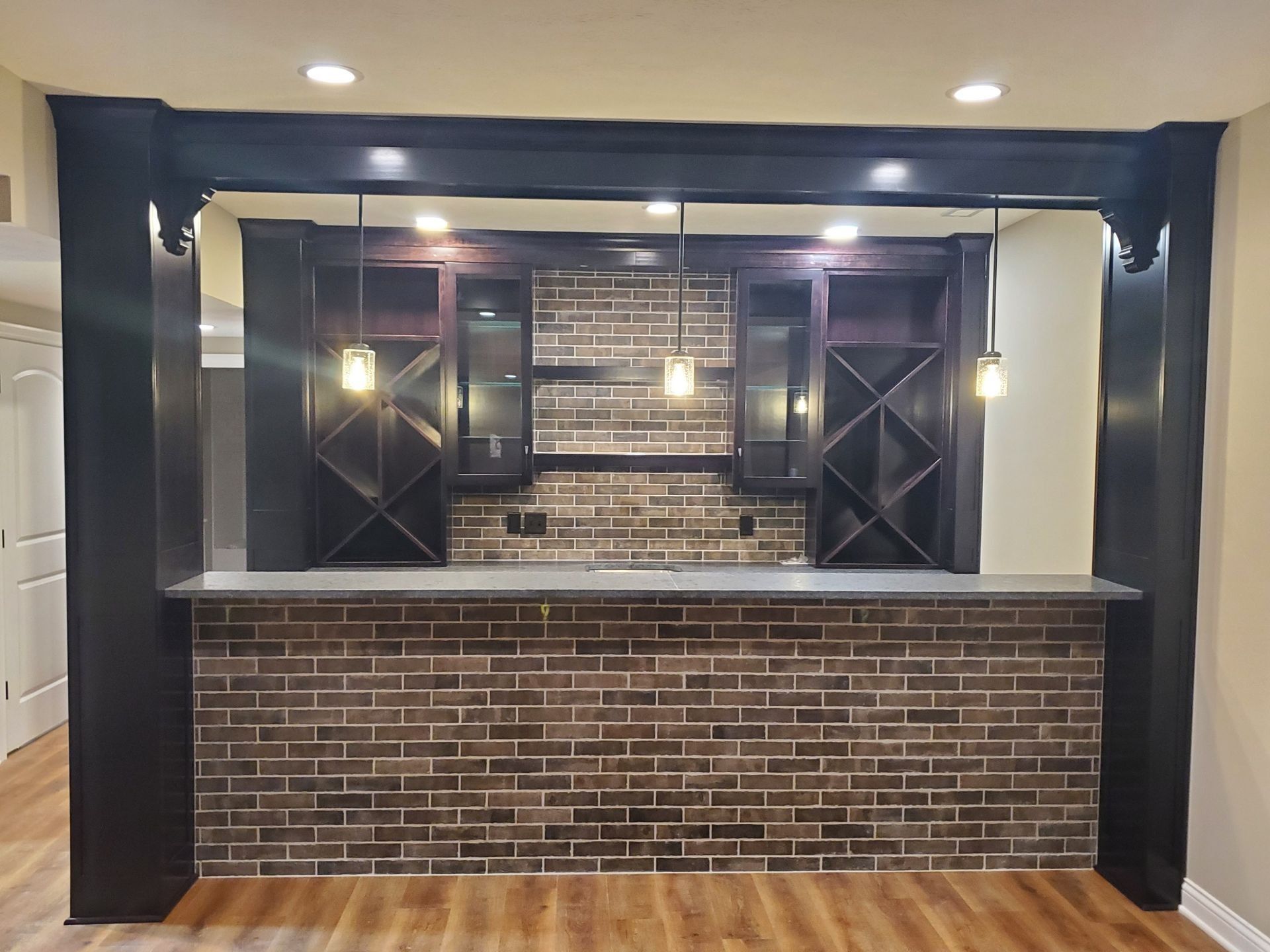 Modern wet bar with brick front, dark wood cabinets, pendant lights, and granite countertop in a finished basement