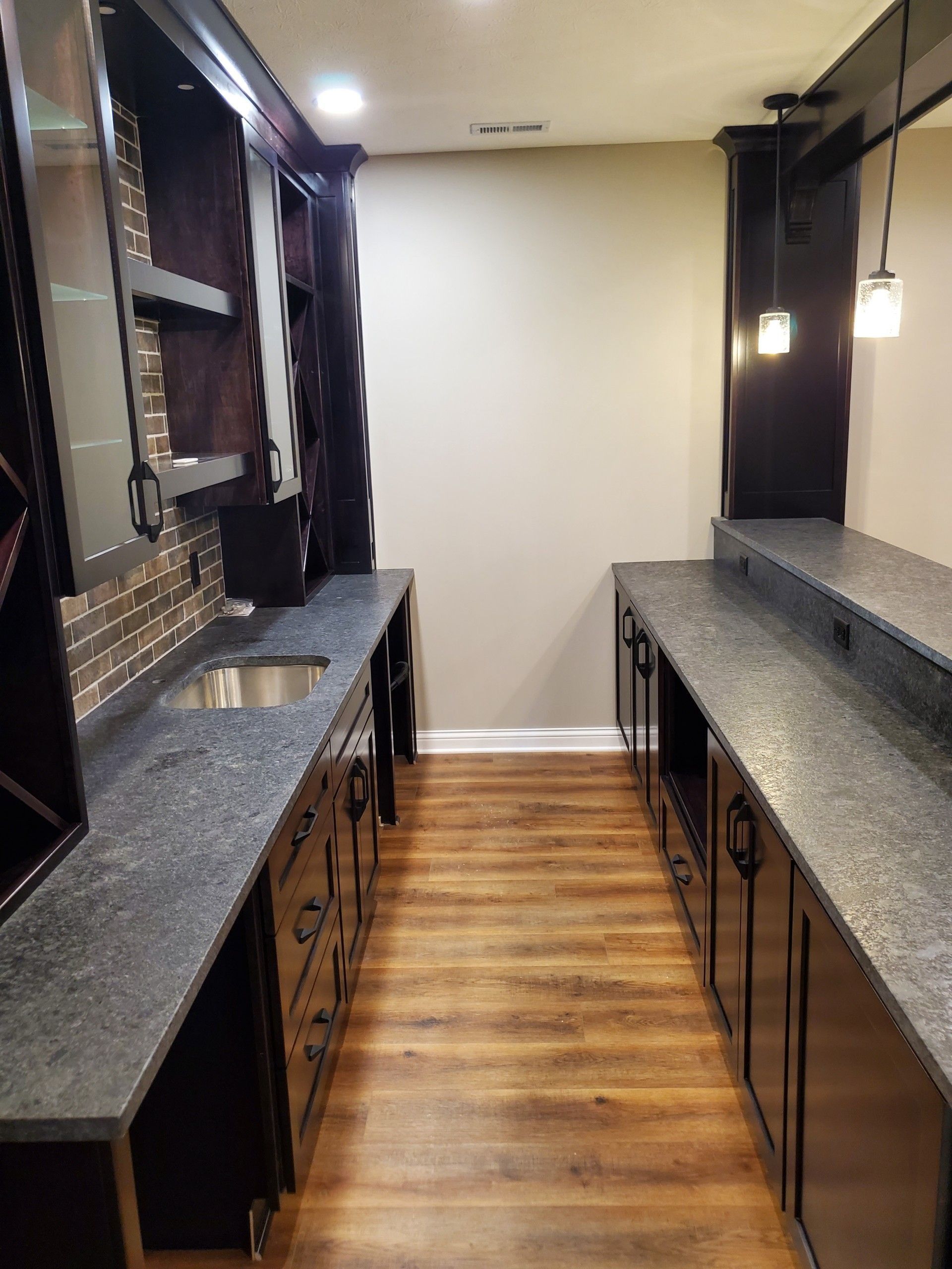 Narrow kitchen galley with dark countertops, black cabinets, and wood floor lighting.