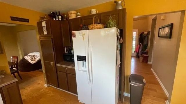 Kitchen with white refrigerator, dark cabinets, and warm yellow walls leading to a hallway