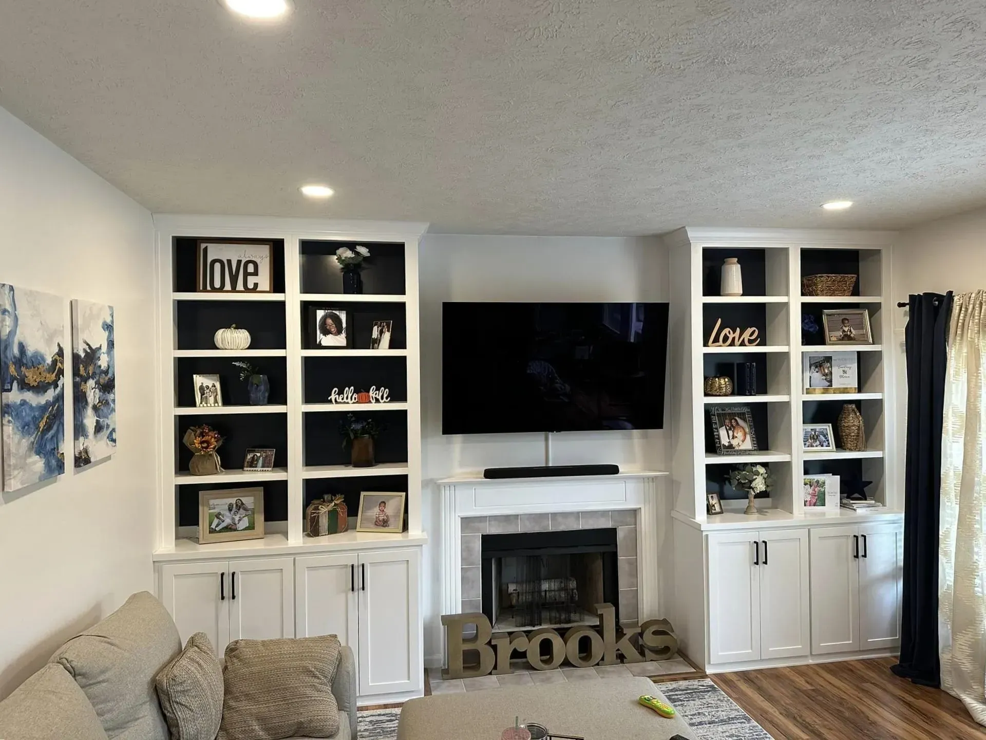Bright living room with built-in shelves, TV over fireplace, couch, and framed decor around a large window