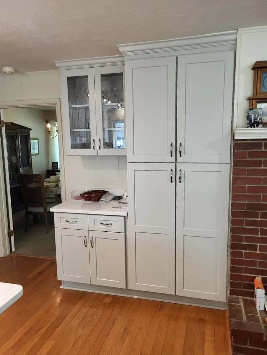 White built-in kitchen hutch with cabinets, drawers, and glass doors beside a brick fireplace in a home interior
