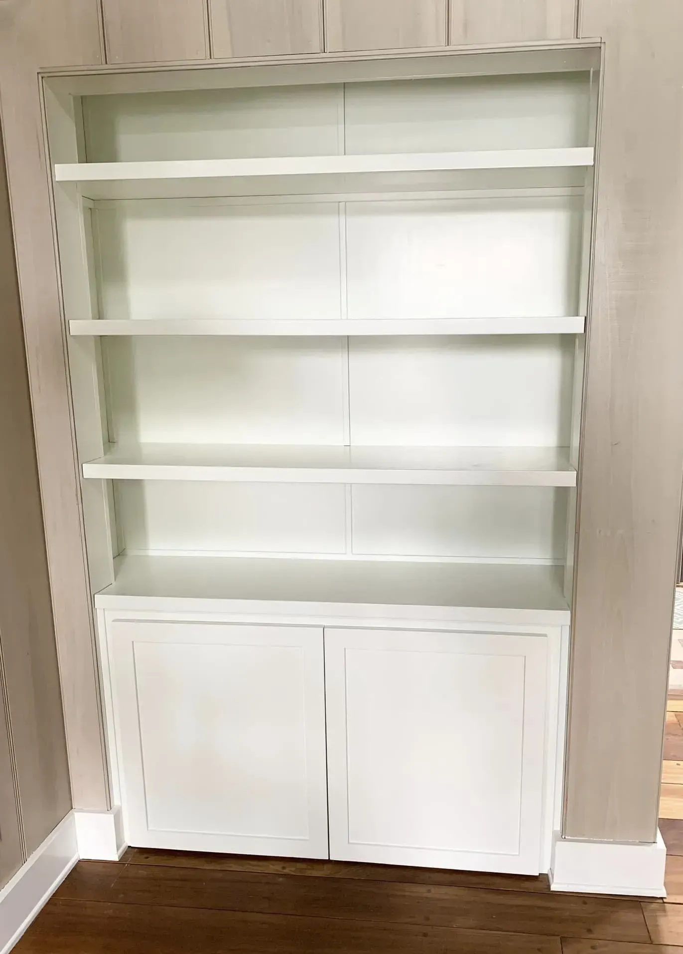 White built-in bookshelf with two lower cabinet doors against a beige wall.