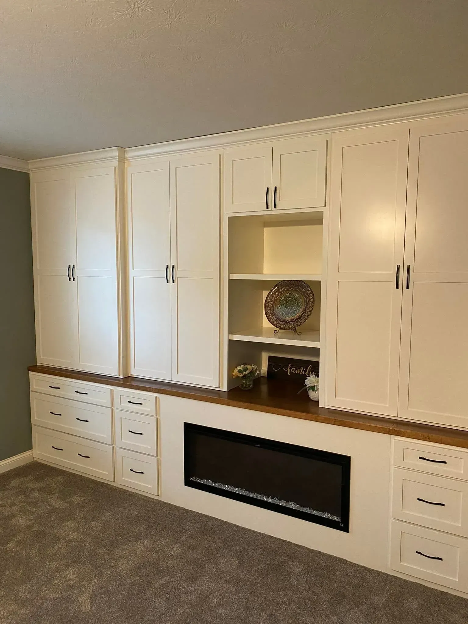 Built-in white cabinets with a central fireplace and open shelves in a carpeted room