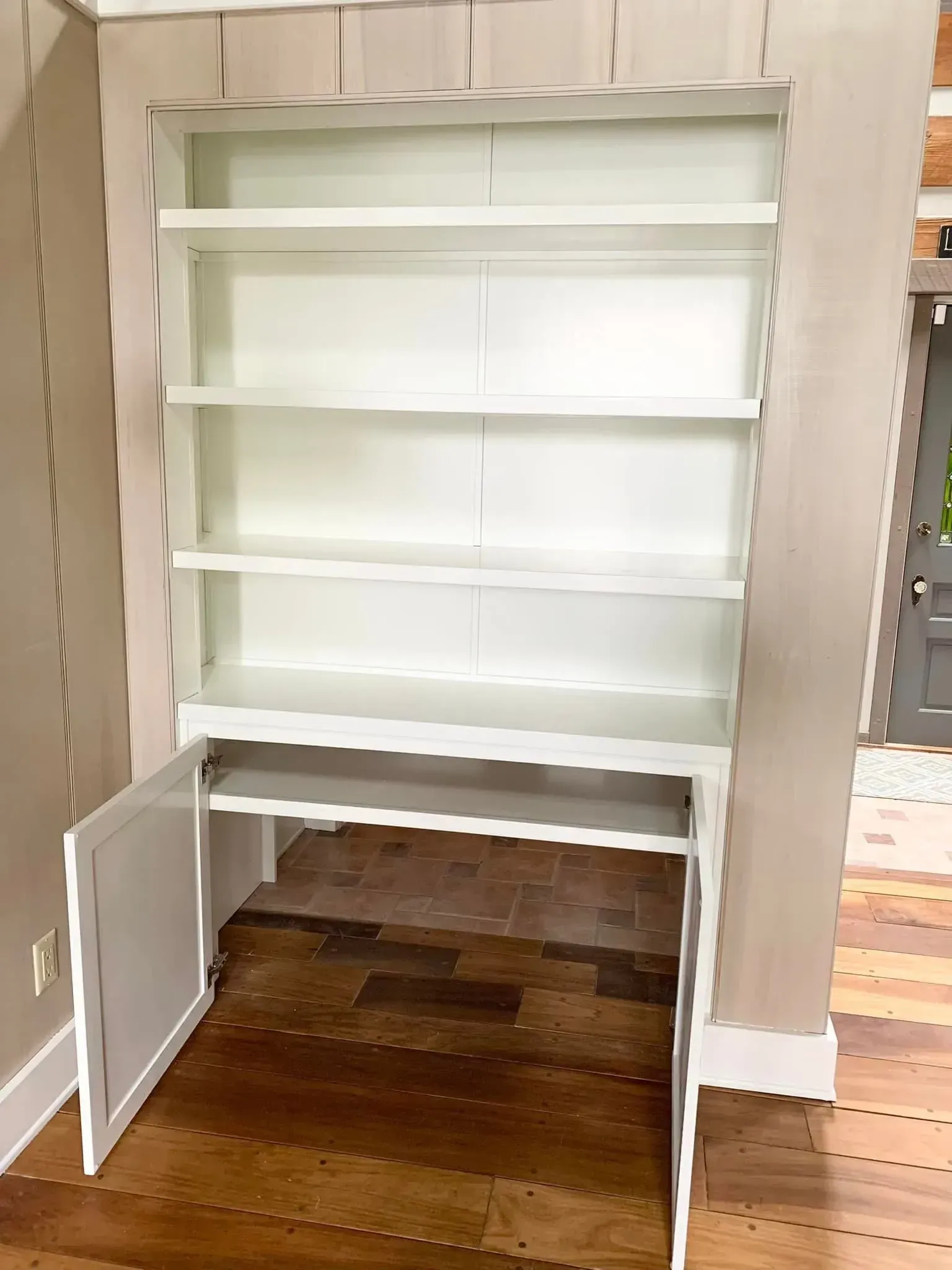 White built-in shelving and cabinet with a lower door open on a hardwood floor.