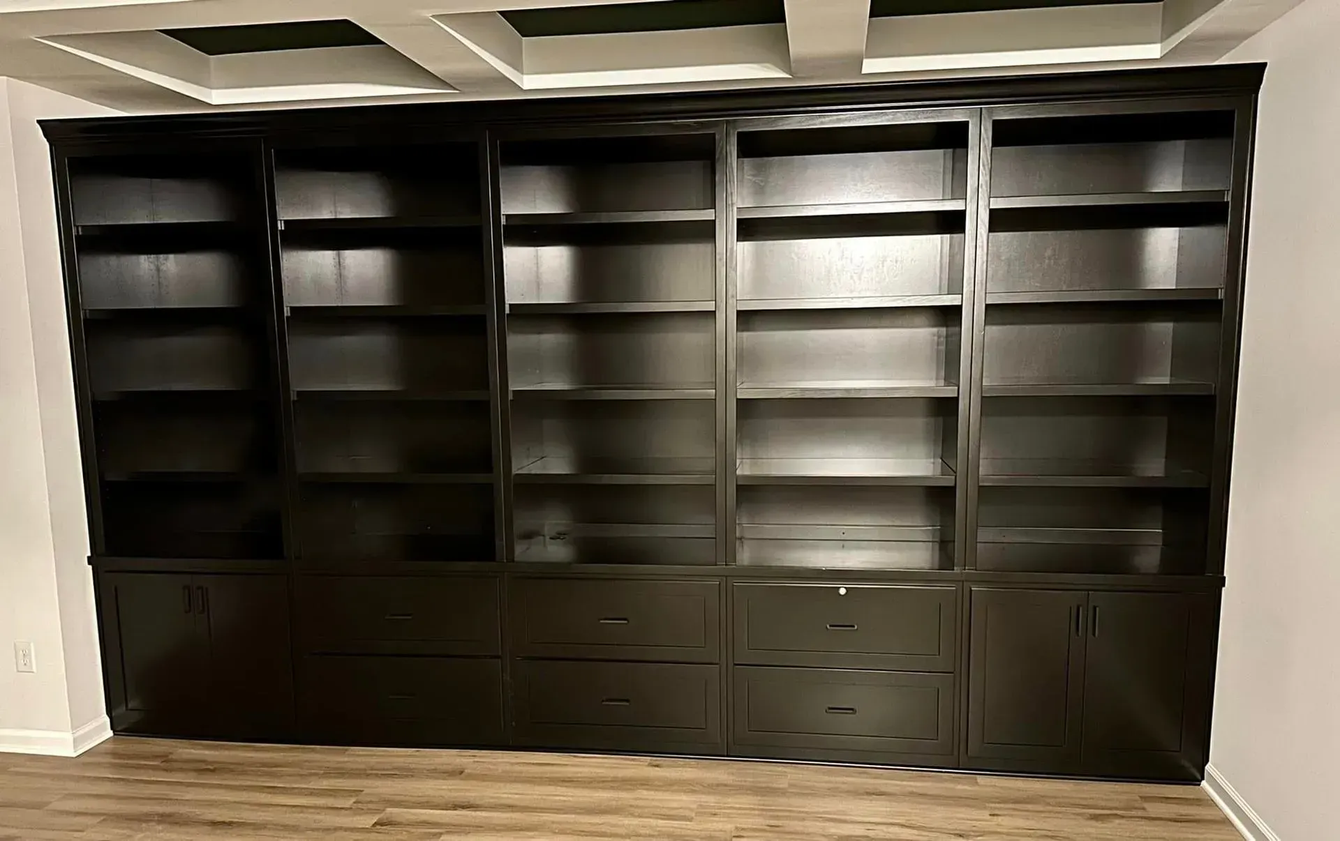 Large dark wood built-in bookshelf with cabinets against a white wall in a room with a coffered ceiling.