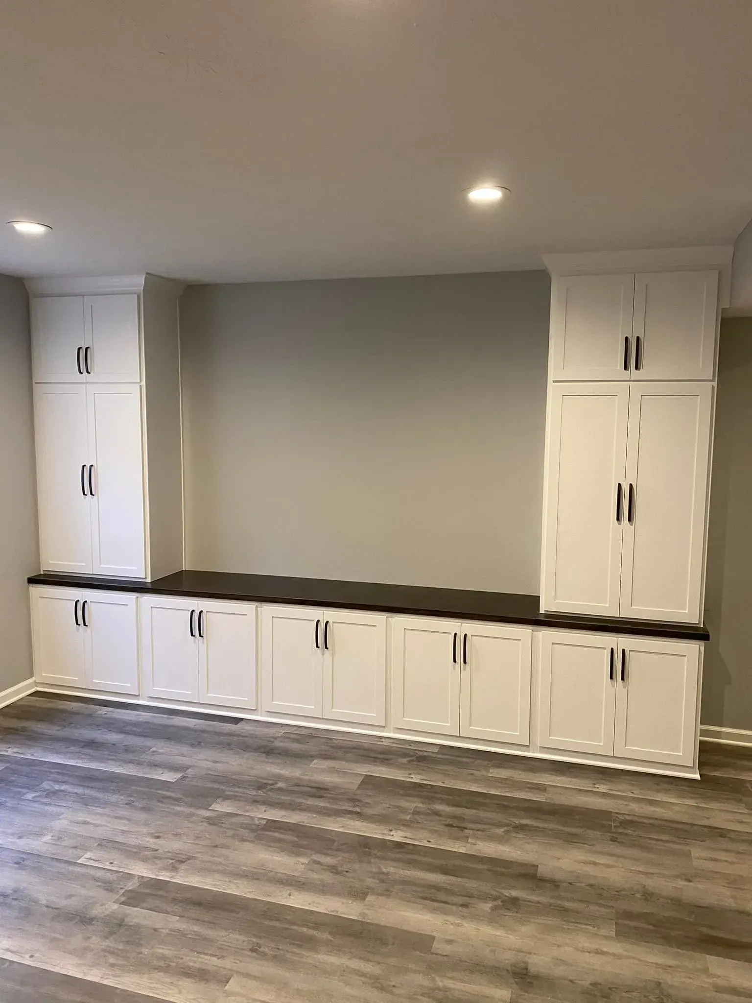 Built-in white cabinets and drawers along a gray wall in a modern room with wood flooring.