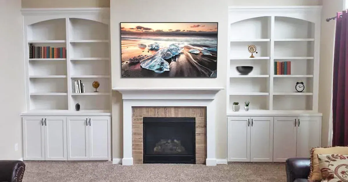 Built-in white shelving and cabinets flanking a fireplace with a wall-mounted landscape TV above it