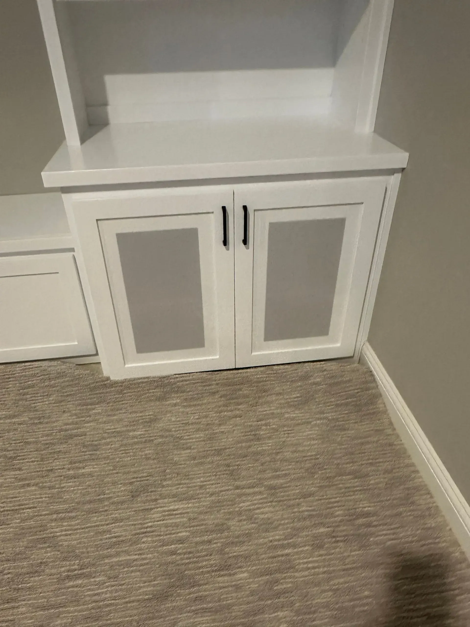 White built-in cabinet with two doors and open shelf in a carpeted room corner