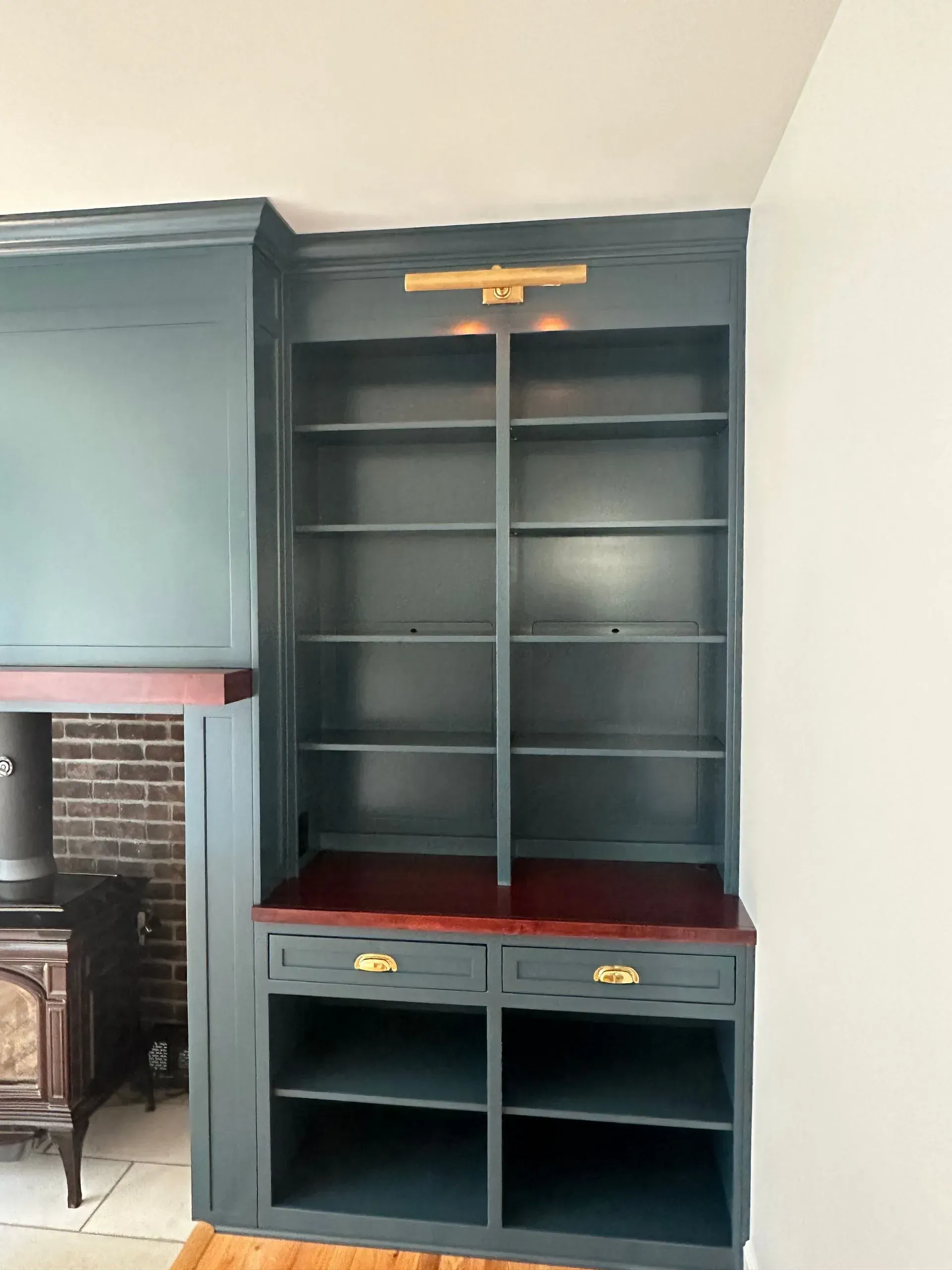 Dark blue built-in cabinet with shelves and drawers beside a fireplace in a room.