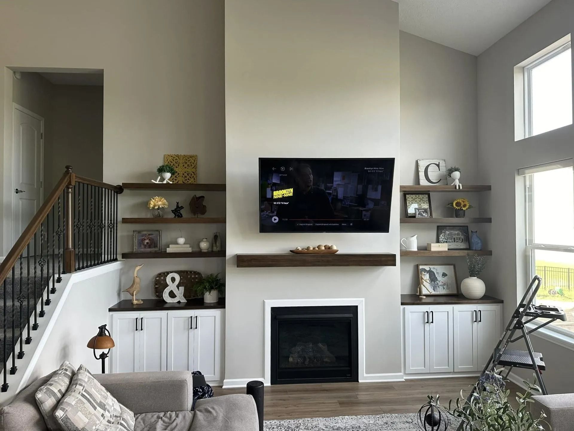 Living room with a wall-mounted TV above a fireplace, built-in shelves, and a staircase on the left.