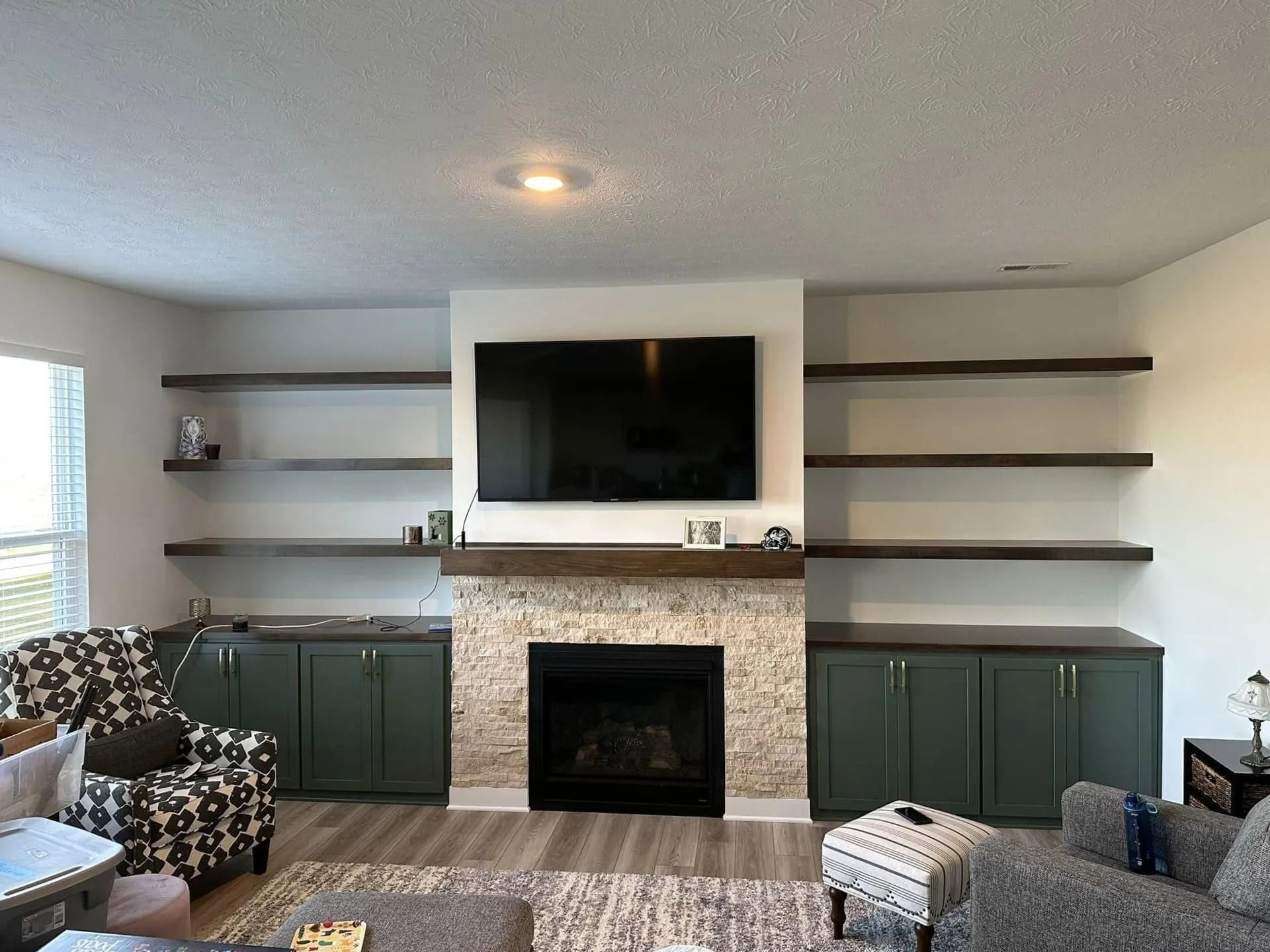 Living room with a fireplace, wall-mounted TV, shelves, and green cabinets under a neutral ceiling.