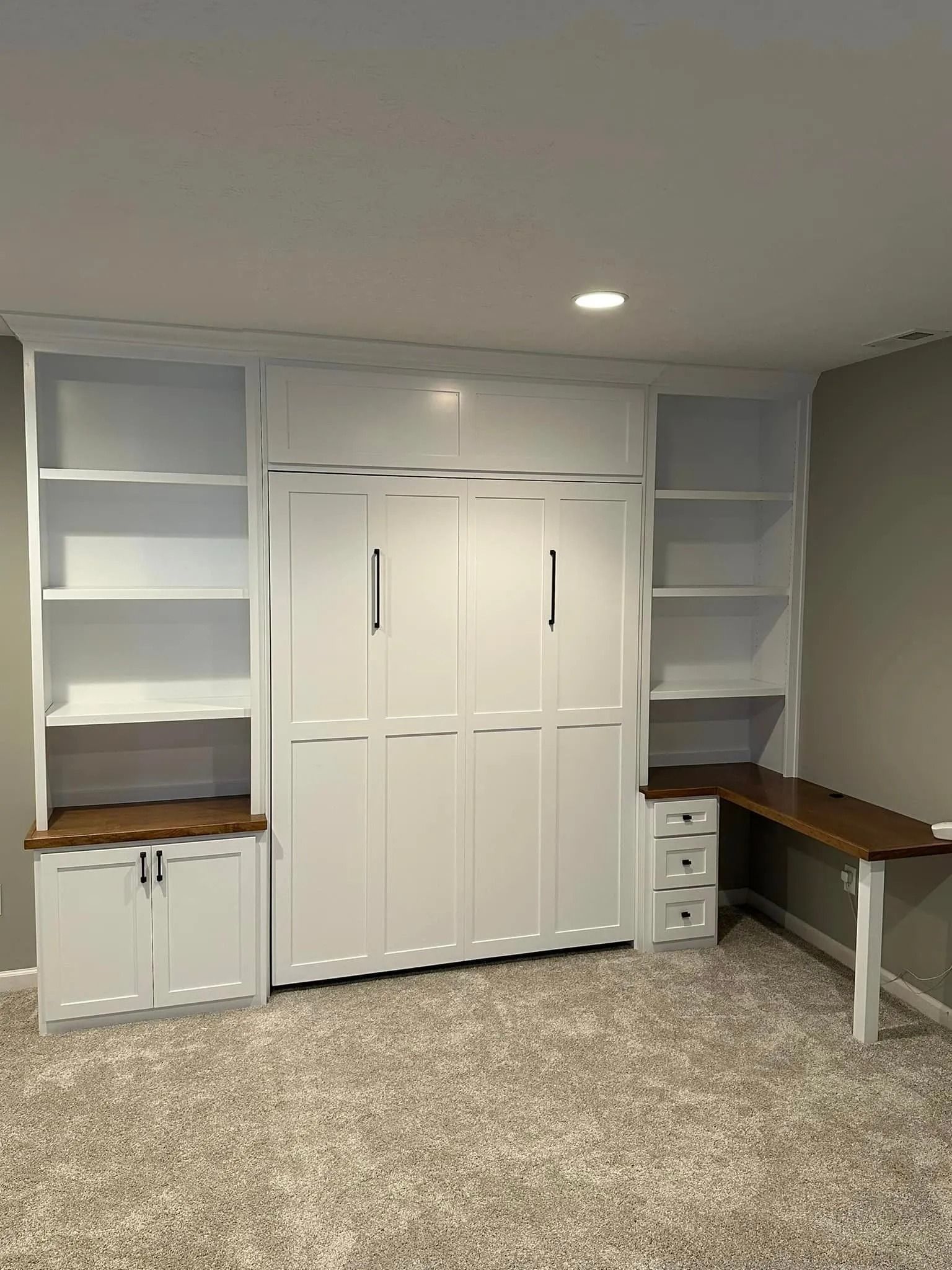 Built-in home office with white cabinets, shelves, and two wood desks on a carpeted floor.