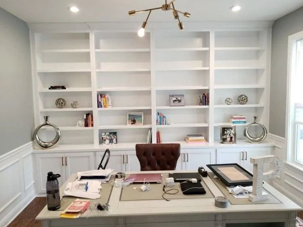 Bright home office with built-in white bookshelves, a large desk, and a tufted brown chair.