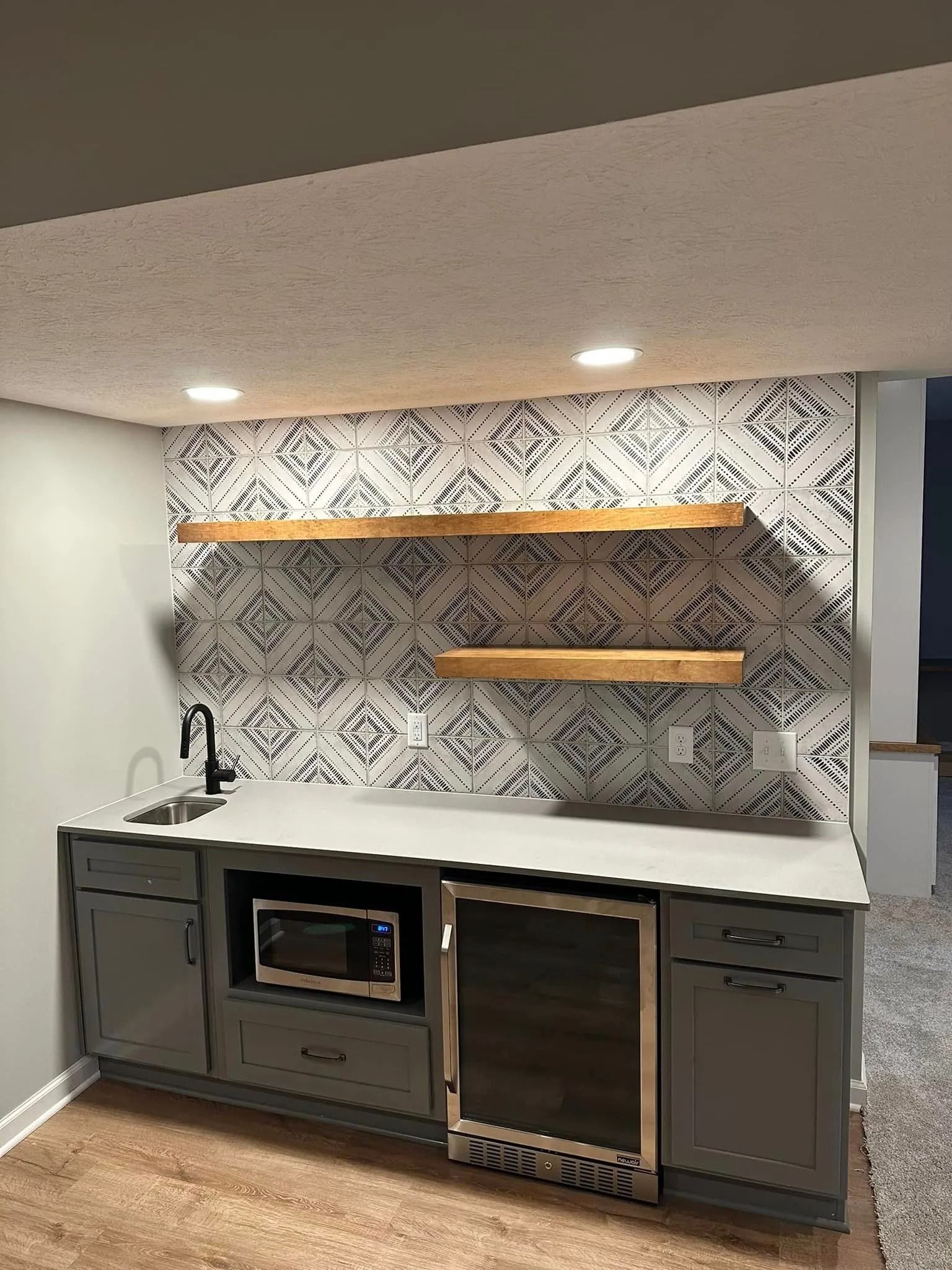Built-in wet bar with gray cabinets, white countertop, wine fridge, sink, and patterned backsplash shelves