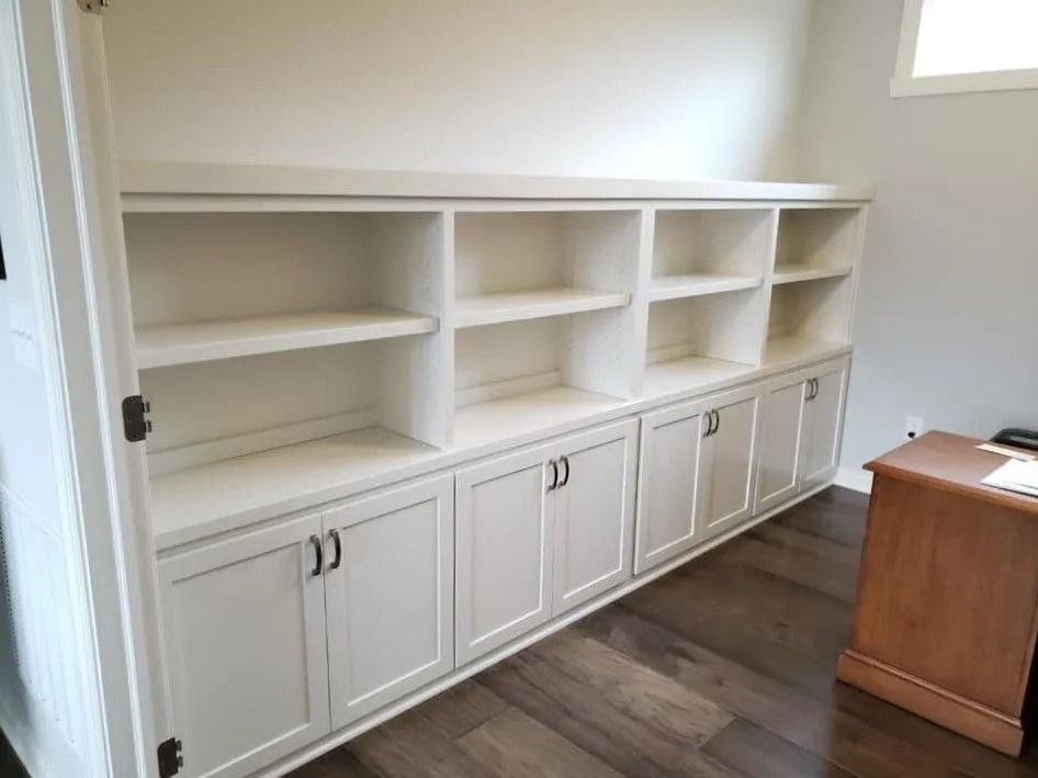 Built-in white shelving and cabinets along a wall in a bright room with wood flooring