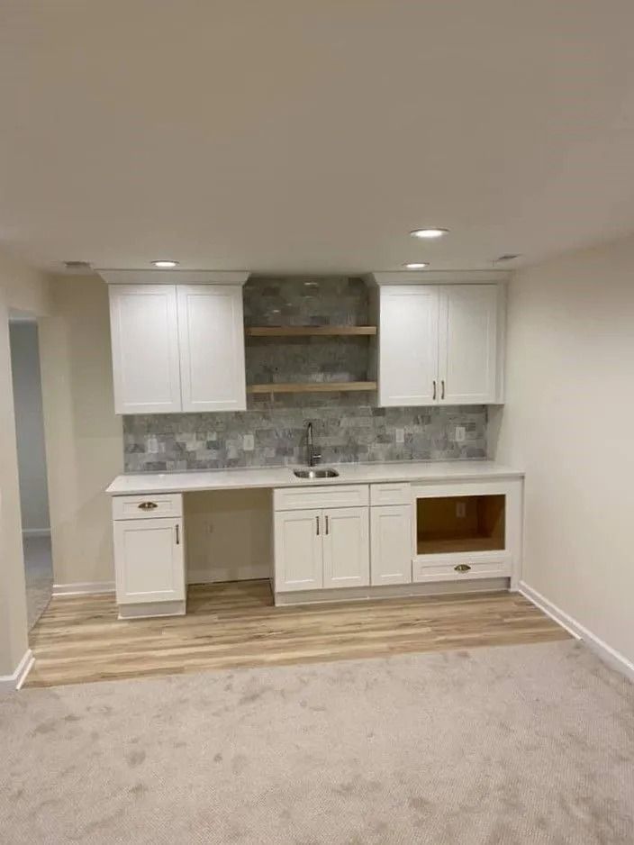 Small white kitchen alcove with cabinets, countertop, sink, and wood-look floor in a carpeted room