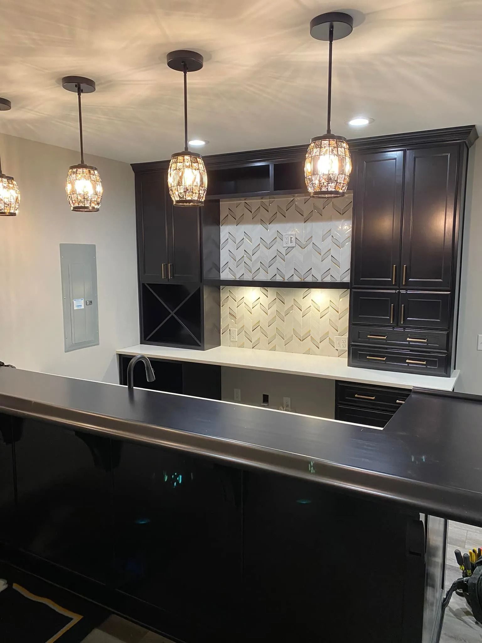 Modern kitchen with black cabinets, white backsplash, and three pendant lights over a dark island