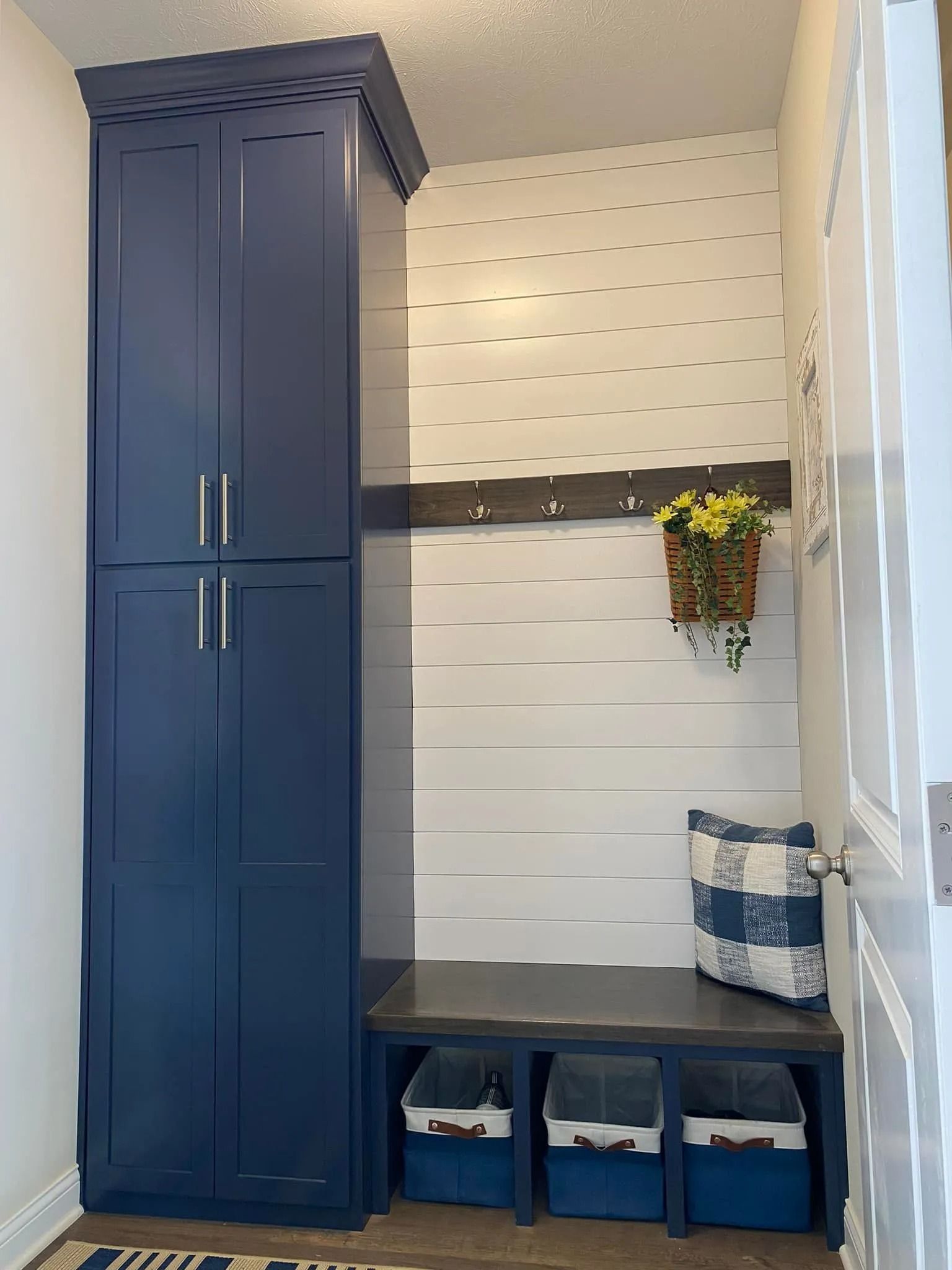 Small mudroom bench with blue storage bins, tall blue cabinet, and white shiplap wall with flowers
