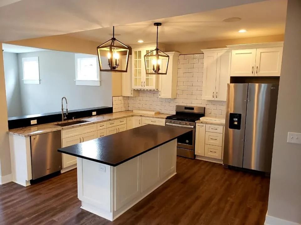 Modern kitchen with dark island, stainless appliances, white cabinets, and wood floors