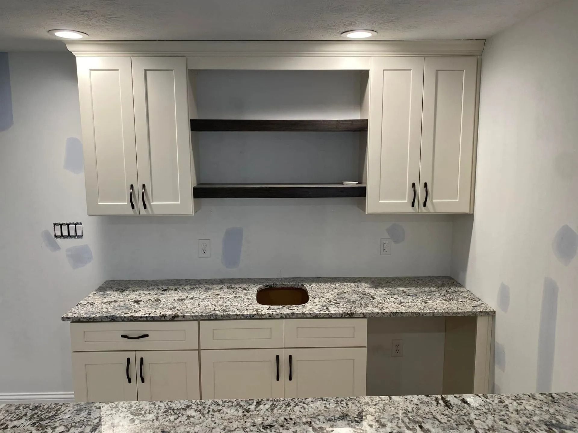 Built-in kitchen cabinets with granite countertop and open shelving in an unfinished room.