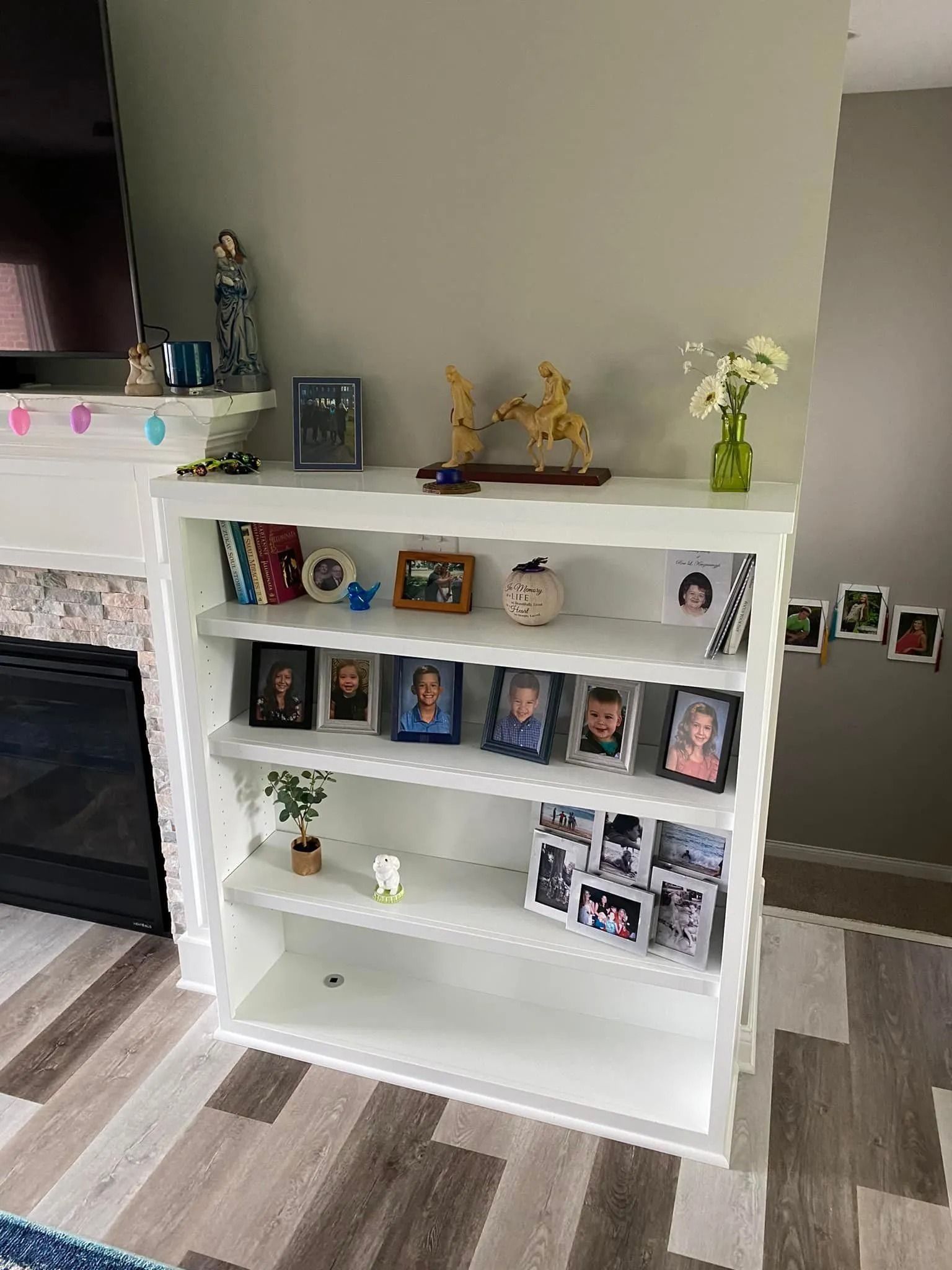 White living room shelving unit with framed photos, small decor, and a fireplace on the left