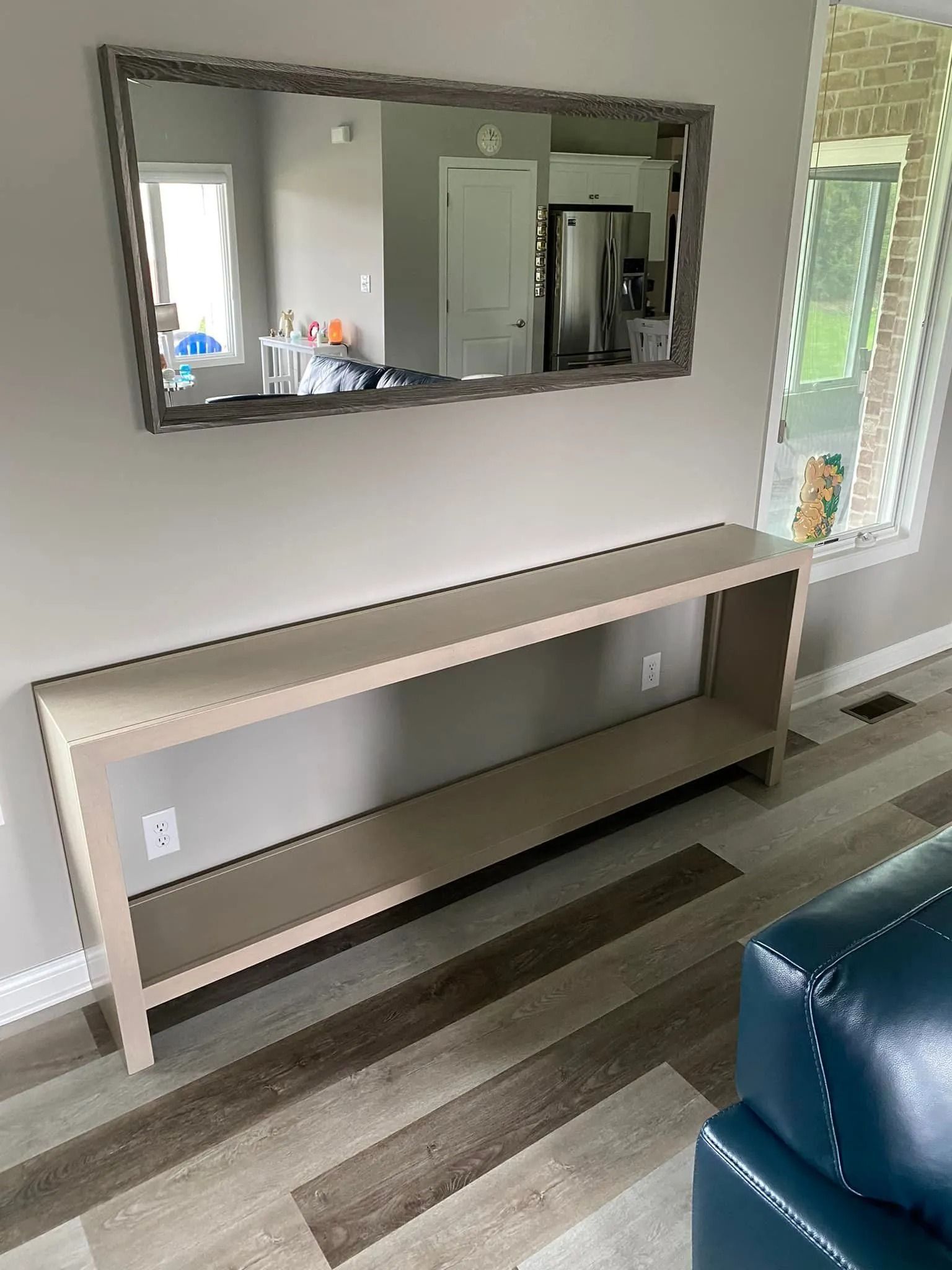 Modern living room console table with mirror, light wall, striped wood floor, and blue chair edge