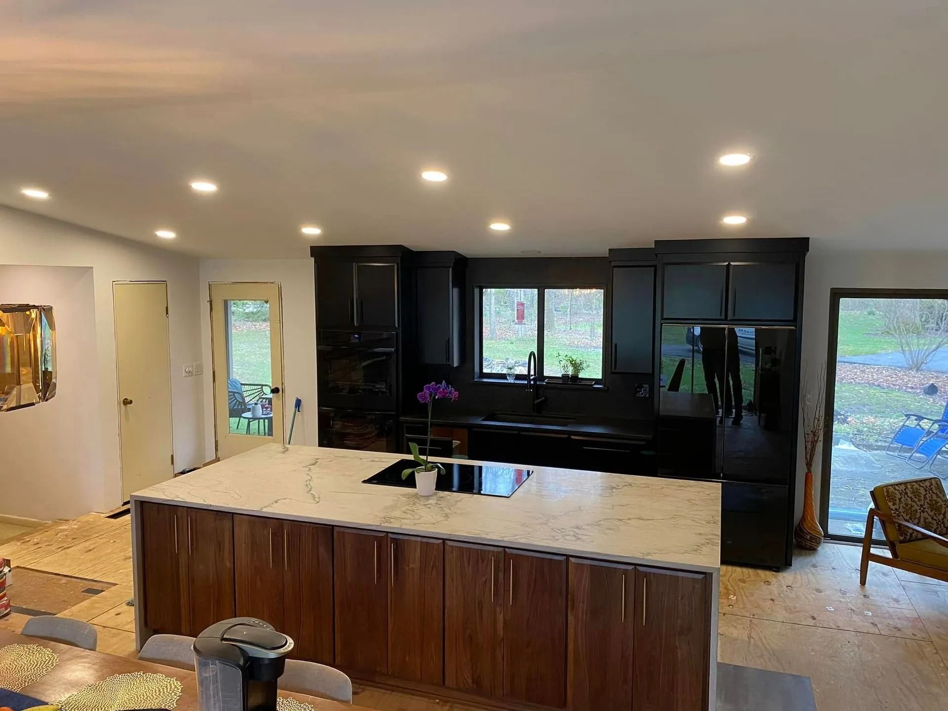 Modern kitchen with dark cabinets, large island, and recessed lighting, under renovation with floor debris.