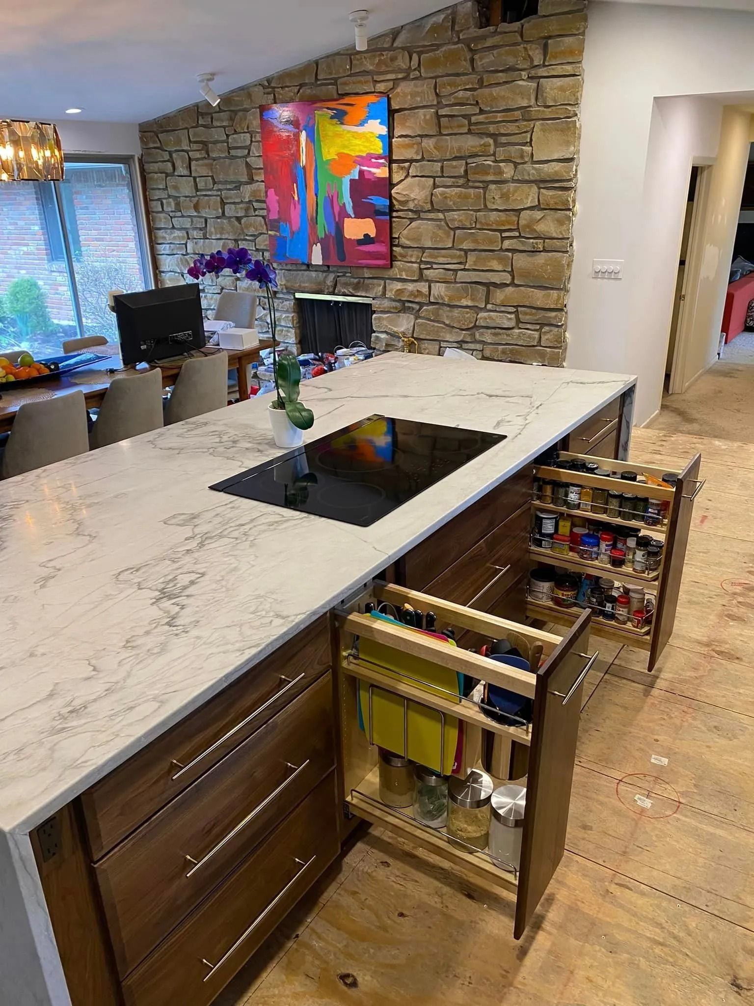Modern kitchen with stone wall, white island, built-in cooktop, and open drawers with utensils.