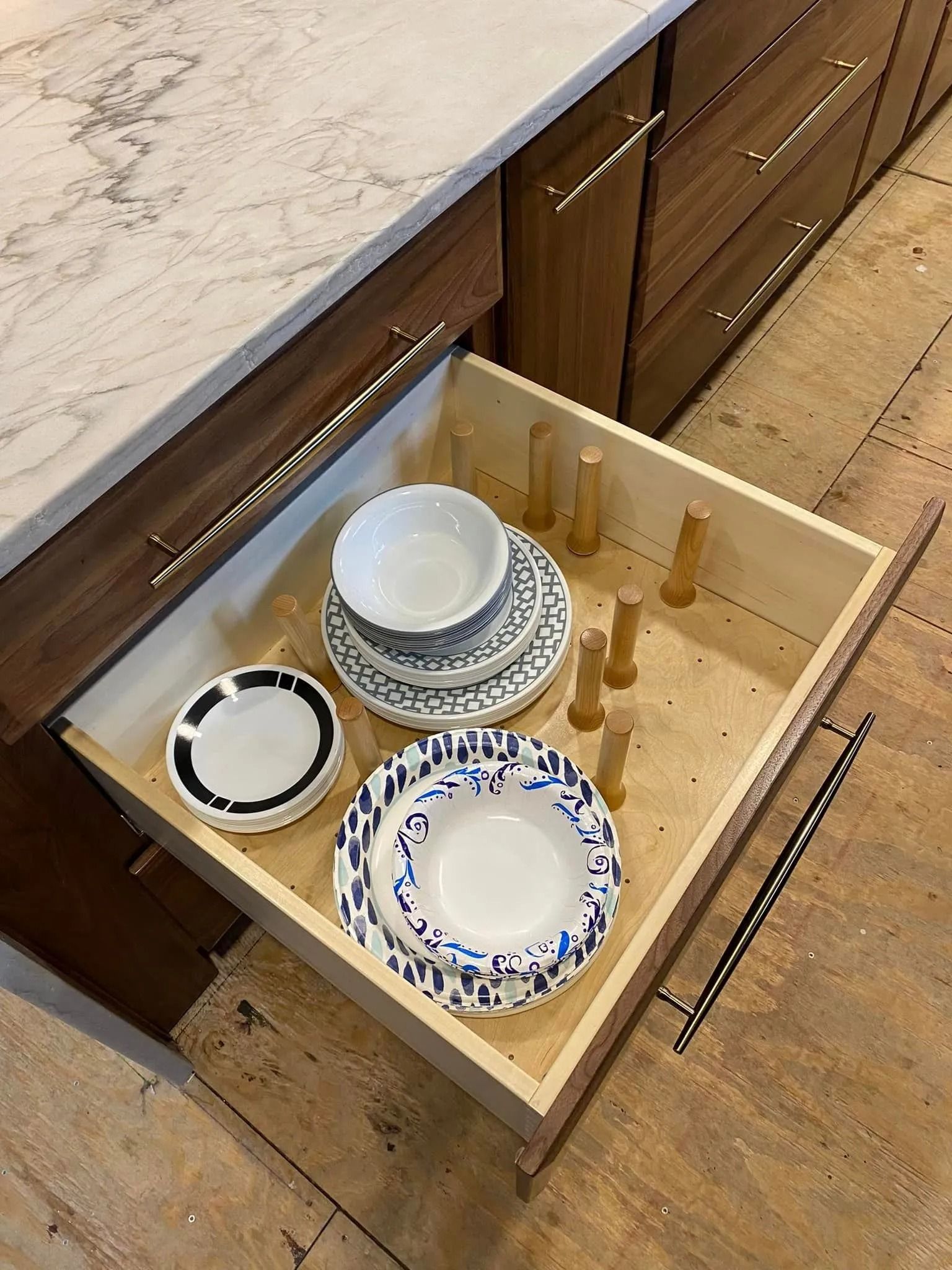 Open kitchen drawer with stacked plates and bowls in a wooden cutlery tray.