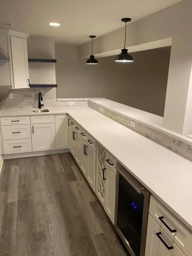 Modern kitchen with white cabinets, gray flooring, black pendant lights, and a long white countertop