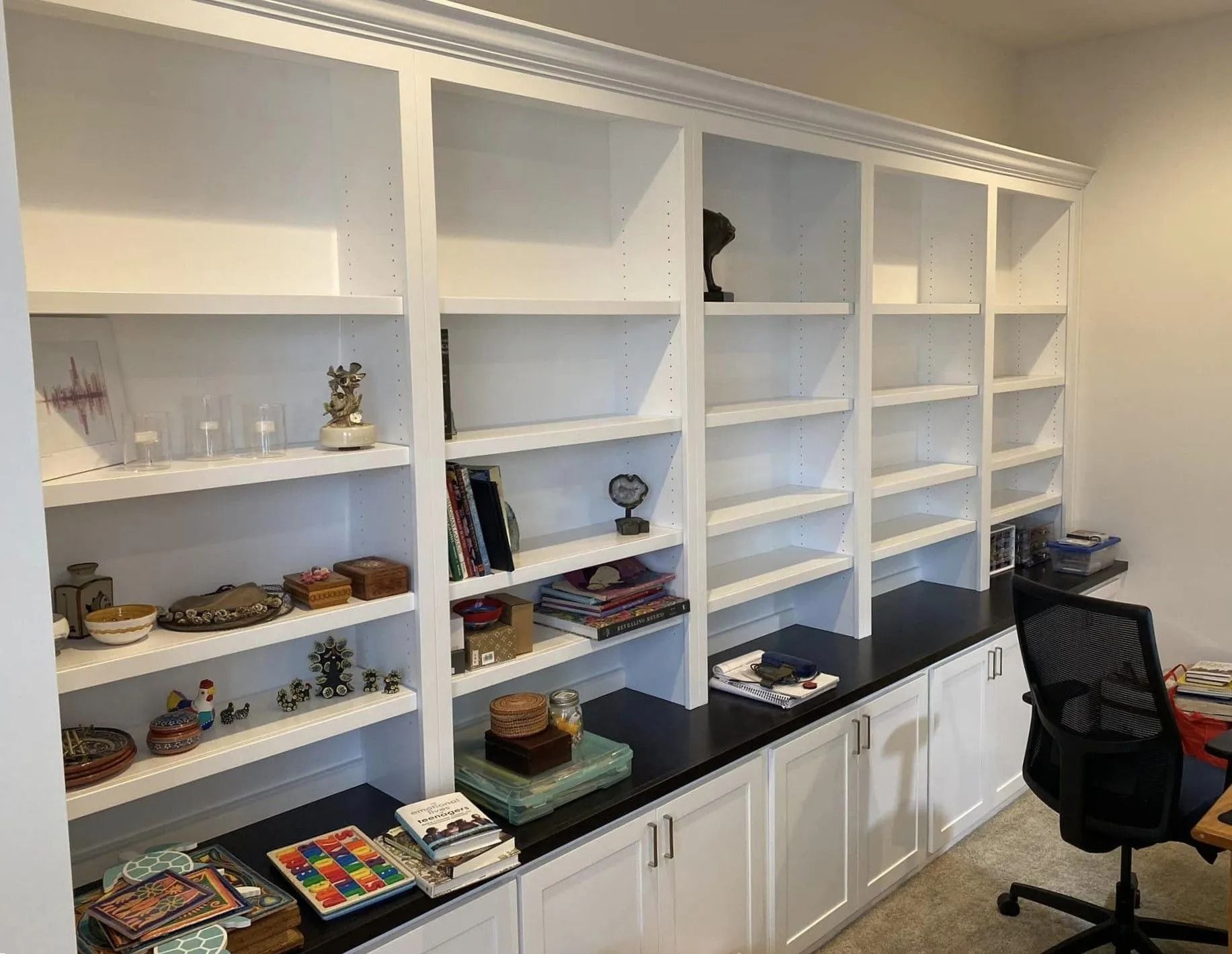 Built-in white bookshelves with books, decor, and games, beside a black desk chair in a home office.