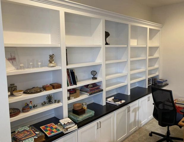 Built-in white bookshelves with books and decor above dark cabinets in a home office.