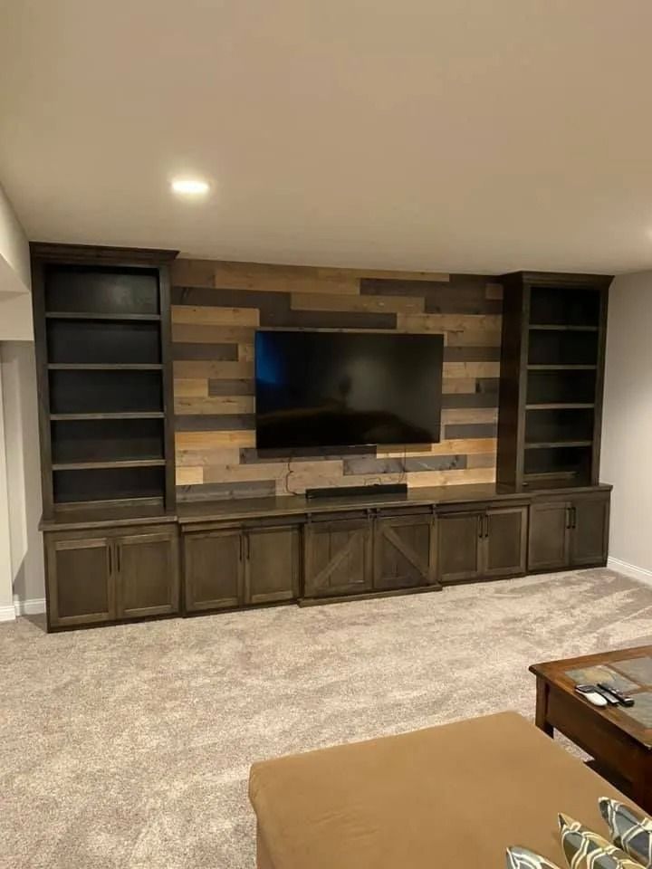 Built-in living room entertainment center with TV, dark shelving, wood paneling, and carpeted floor