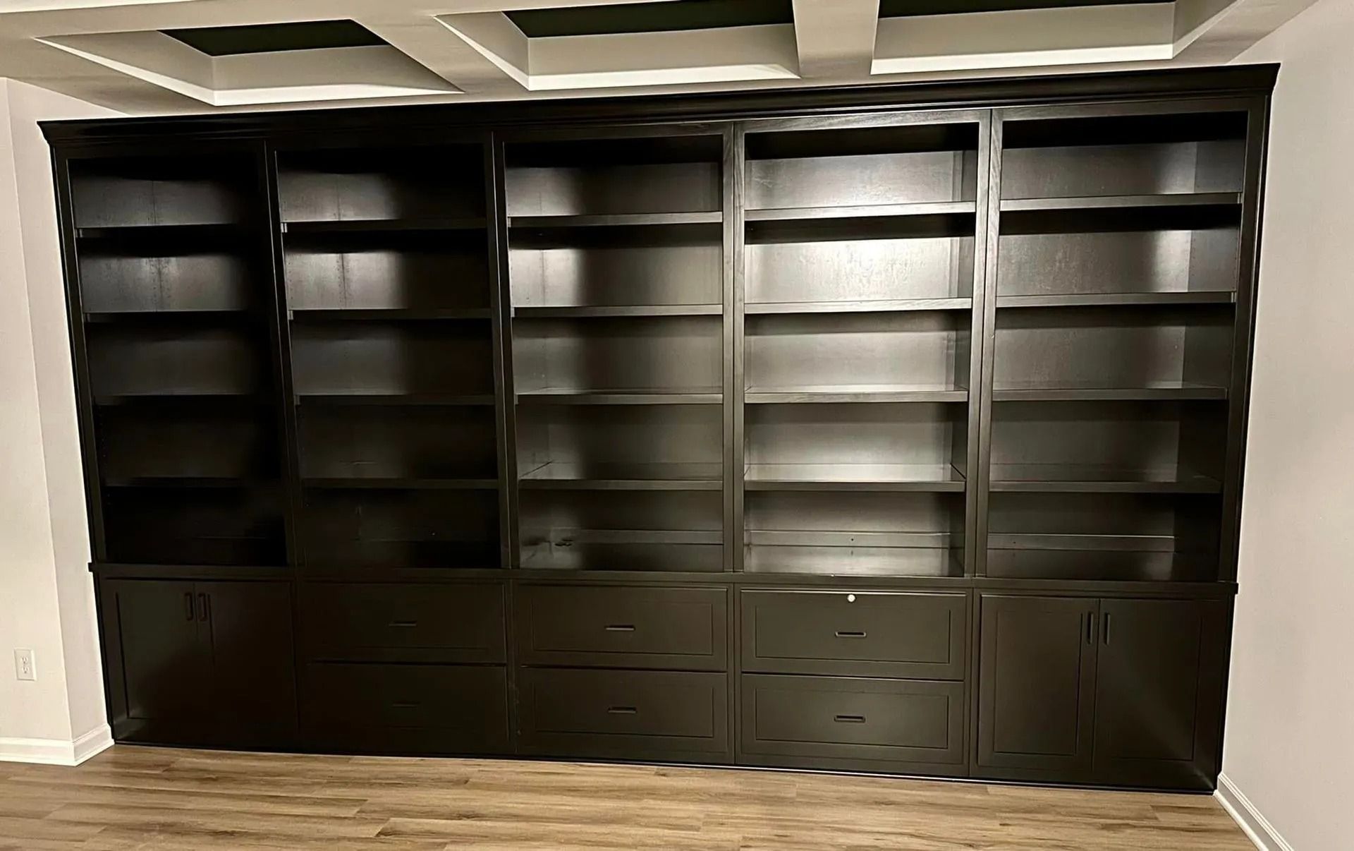 Built-in dark wood bookshelves with drawers against a light wall in an empty room